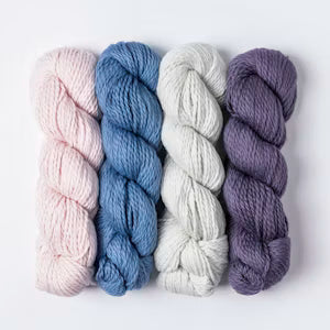 Four skeins of twisted yarn in pastel shades of pink, blue, off-white, and lavender-purple, arranged side by side on a plain white background.