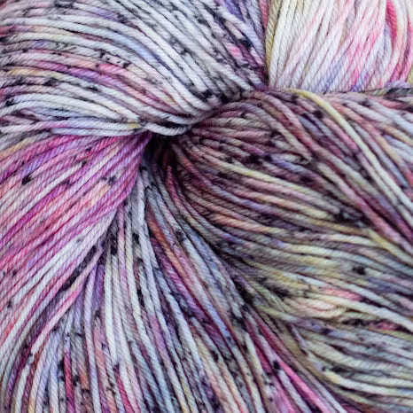Close-up of a variegated skein of yarn with blended pastel pink, purple, cream, and gray tones with small dark flecks.