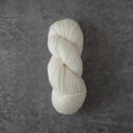 A single skein of soft off-white yarn photographed from above on a textured dark gray surface.