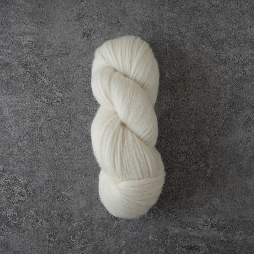 A single skein of soft off-white yarn photographed from above on a textured dark gray surface.