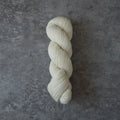 A single skein of cream-colored yarn twisted into a braid, displayed vertically on a textured gray concrete surface.