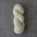 A skein of cream-colored yarn resting on a textured gray surface.