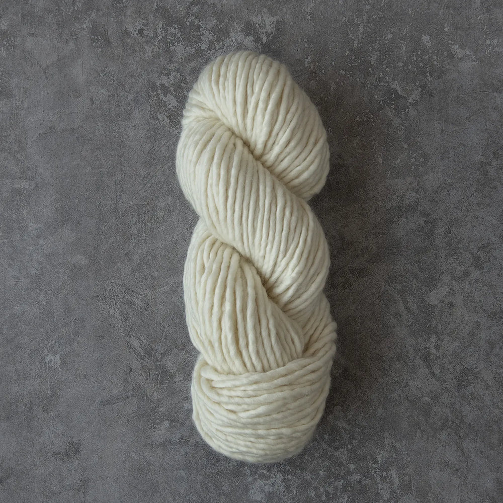 A skein of cream-colored yarn resting on a textured gray surface.