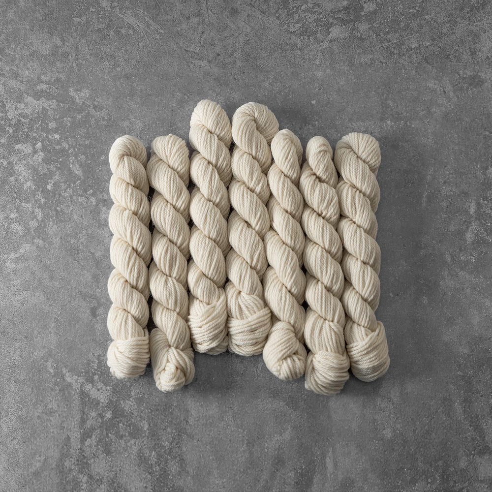 Set of six skeins of cream-colored yarn on a gray surface
