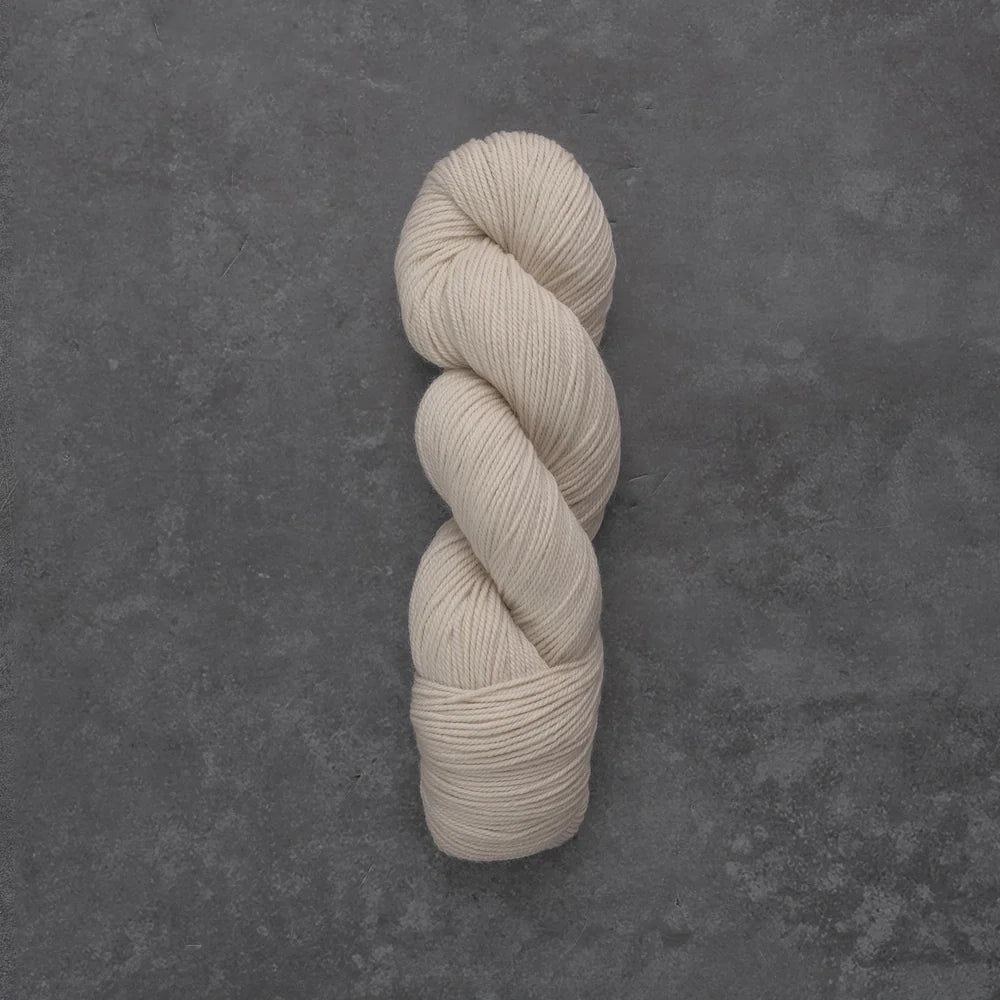 A single skein of cream-colored yarn twisted into a hank, displayed vertically on a textured dark gray slate surface.