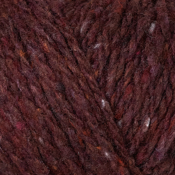 A close-up of variegated yarn in a deep burgundy and brown colorway, showing the fuzzy texture of the twisted plies and subtle flecks of lighter and warmer tones.