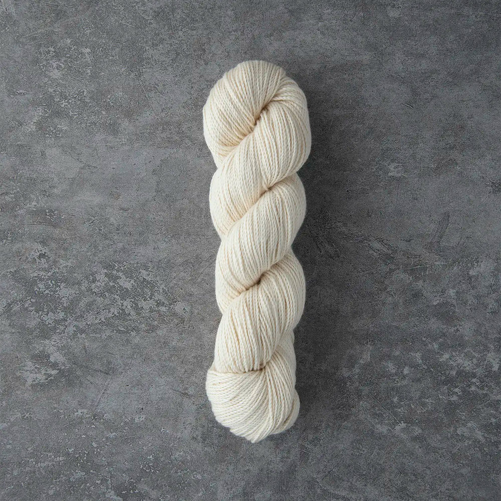 A single skein of cream-colored yarn standing vertically on a textured gray surface.
