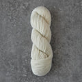 A single skein of cream-colored yarn twisted into a balm, displayed vertically on a textured gray concrete surface.