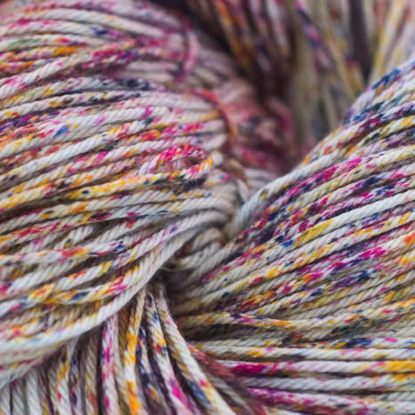 Close-up of variegated yarn with a speckled multicolor pattern of pink, yellow, blue, and purple on a cream base.