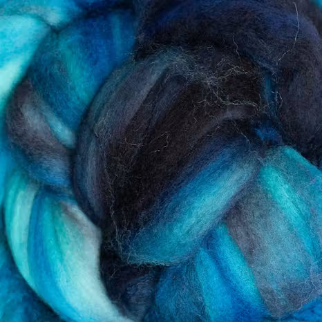 A close-up of fluffy fiber roving or yarn in a variegated blend of deep navy, blue, teal, and aqua tones.
