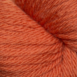 A close-up of soft, twisted yarn in a warm rust or burnt orange color, filling the entire frame.