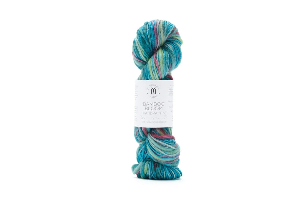 A single skein of Bamboo Bloom Handdye yarn with a white paper label, featuring variegated colors of teal, blue, green, and pink, set against a plain white background.