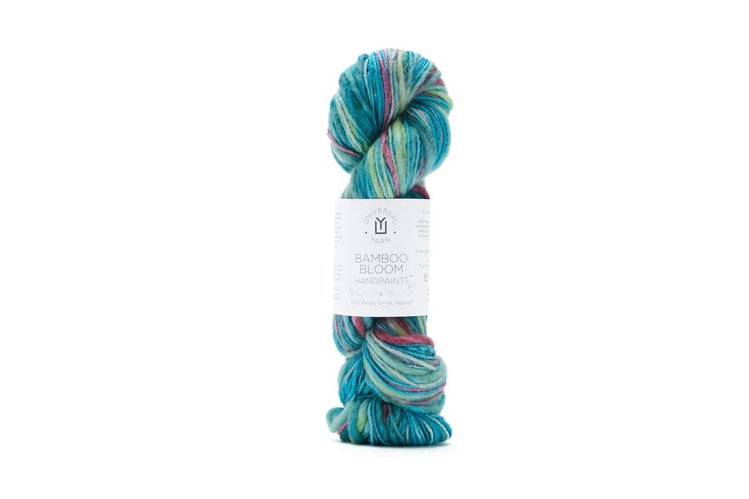 A single skein of Bamboo Bloom Handdye yarn with a white paper label, featuring variegated colors of teal, blue, green, and pink, set against a plain white background.