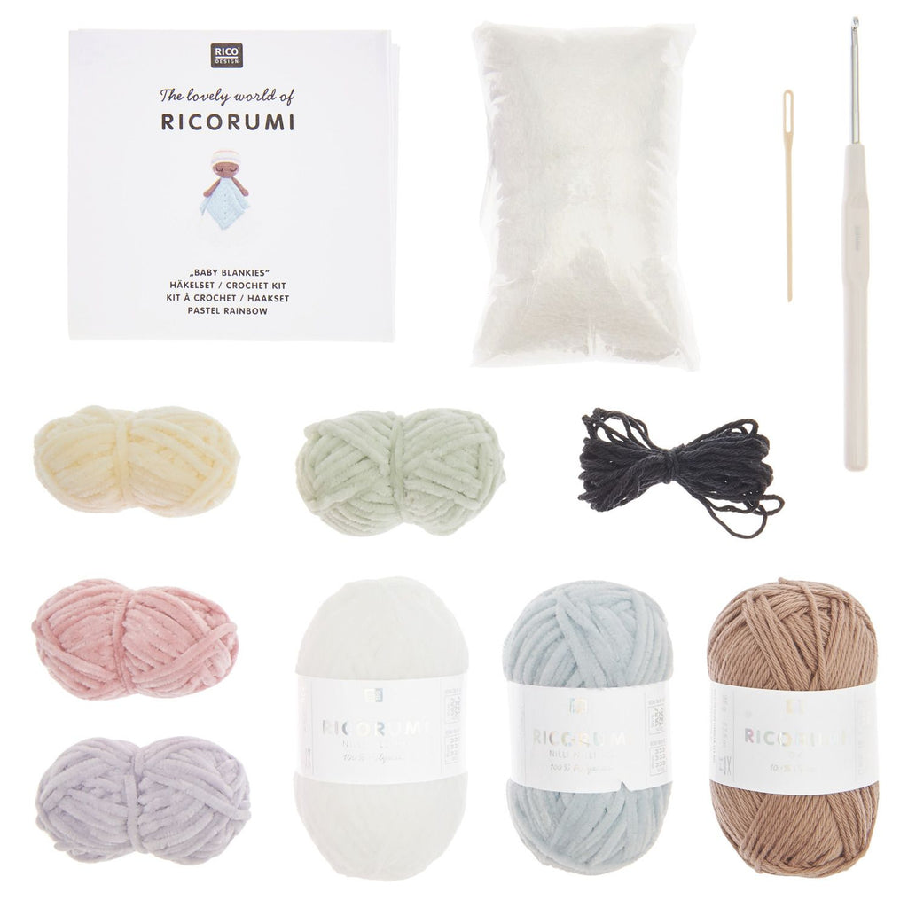 Ricorumi Baby Blanket Kit contents arranged on a white background, including a printed booklet, a white fuzzy blanket, a wooden hook, and six balls of yarn in cream, pale green, black, pink, white, light blue, and taupe.