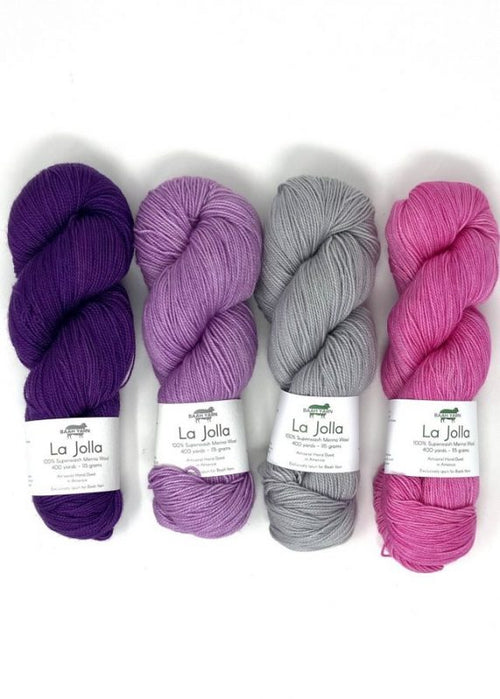 Four skeins of La Jolla yarn in purple, lavender, gray, and pink, arranged side by side on a white background.