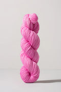 A single skein of bright pink yarn standing upright against a clean, light gray studio background.