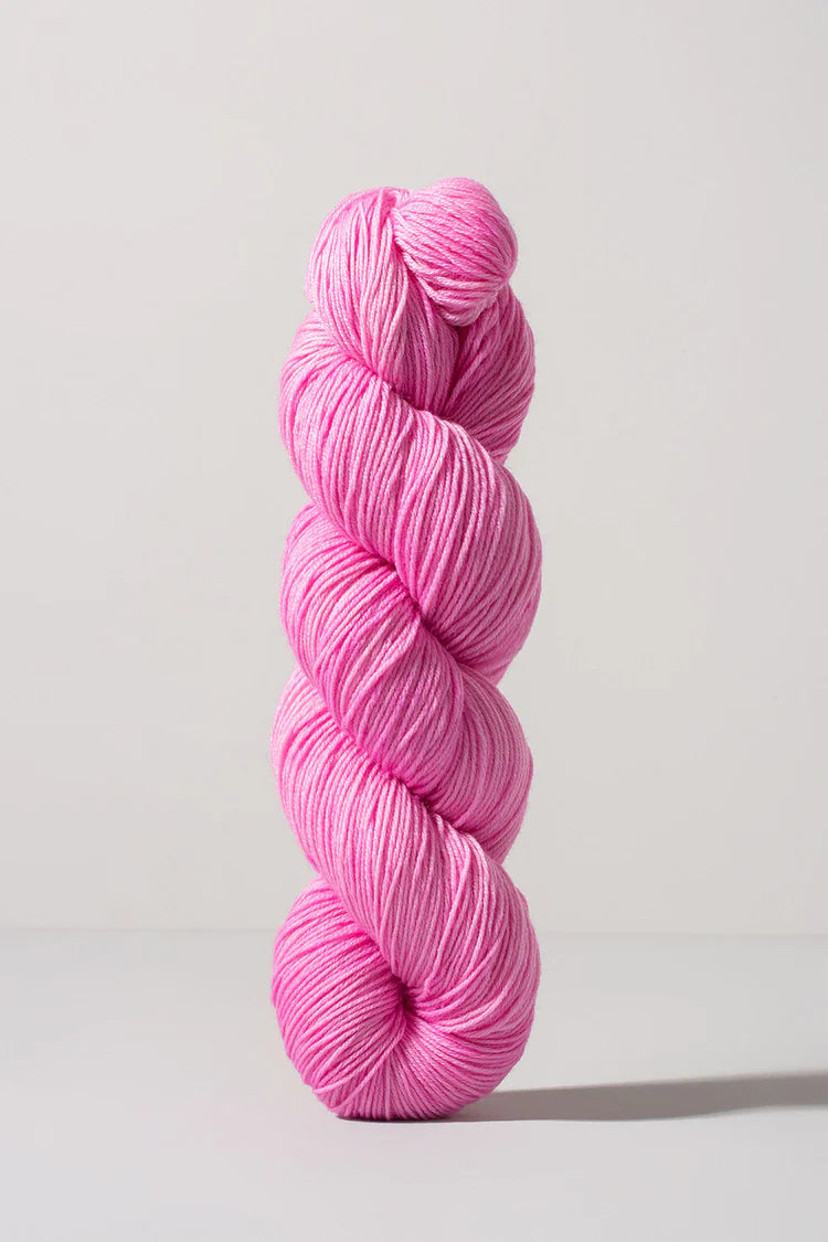 A single skein of bright pink yarn standing upright against a clean, light gray studio background.
