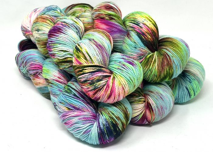 A pile of hand-dyed hanks of yarn in a variegated multicolor pattern of mint green, turquoise, pink, purple, yellow, and black on a white background.