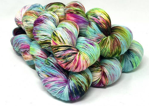 A pile of hand-dyed hanks of yarn in a variegated multicolor pattern of mint green, turquoise, pink, purple, yellow, and black on a white background.