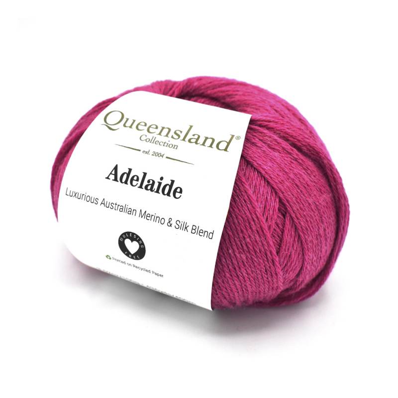 A ball of magenta-pink yarn wrapped with a white paper label reading 'Queensland Collection Adelaide Luxury Australian Merino & Silk Blend'.