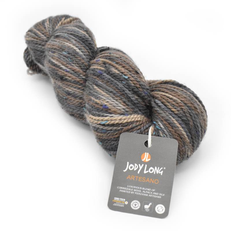 A skein of Jody Long Artesano yarn in a variegated blend of gray, brown, beige, and muted blue, with its brand tag attached, on a plain white background.