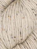 Close-up of a skein of chunky yarn in a warm oatmeal beige color, featuring small dark brown and black flecks throughout the plied texture.