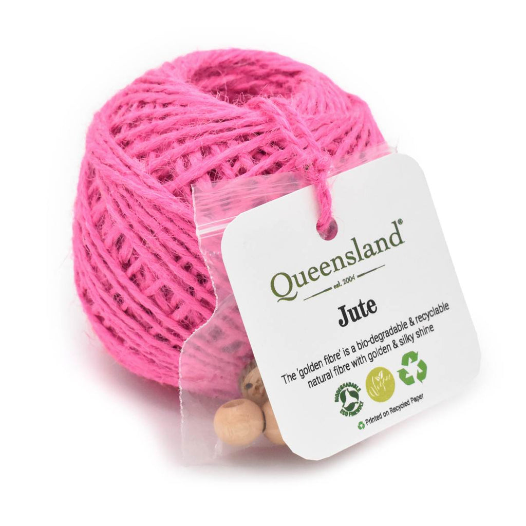 A ball of bright pink jute twine wrapped in a clear plastic sleeve with a white product tag that reads 'Queensland Jute' and shows small wooden beads at the bottom.