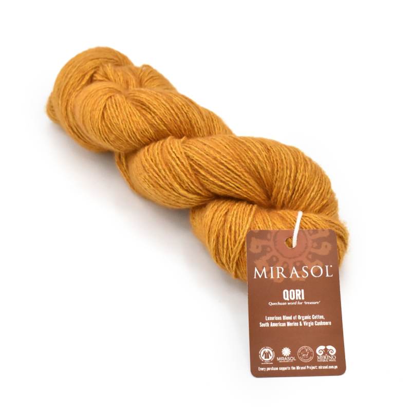 A skein of Mirasol Qori yarn in a warm mustard-gold color, with its brown paper label attached, on a clean white background.