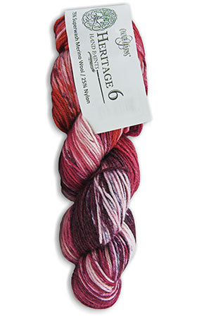 A skein of Heritage 6 yarn from Wild Horse Yarn, featuring variegated colors of deep red, pink, purple, and white, with its paper label attached.