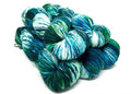 A pile of variegated hank yarns in shades of teal, blue, green, and white, photographed on a clean white background.