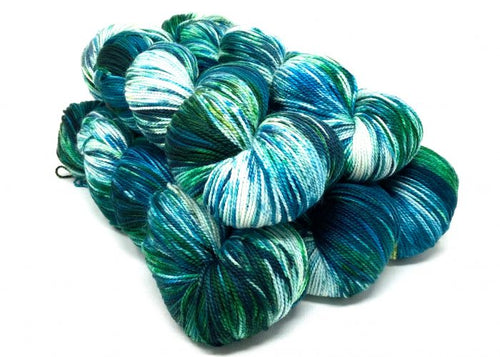 A pile of variegated hank yarns in shades of teal, blue, green, and white, photographed on a clean white background.