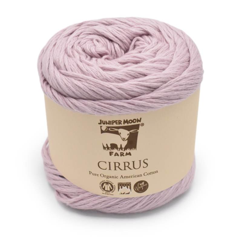 A skein of Juniper Moon Farm Cirrus yarn in a soft dusty lavender-pink color, wrapped in a beige paper label.