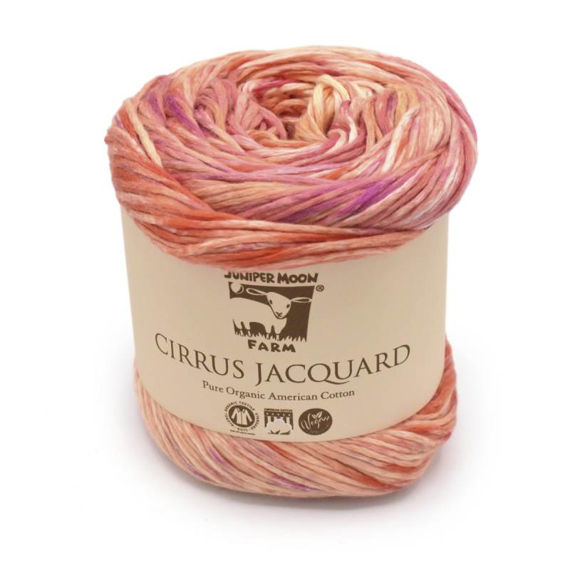 A skein of Jumper Moon Cirrus Jacquard yarn in a variegated blend of peach, pink, orange, and purple, wrapped in a beige paper label.