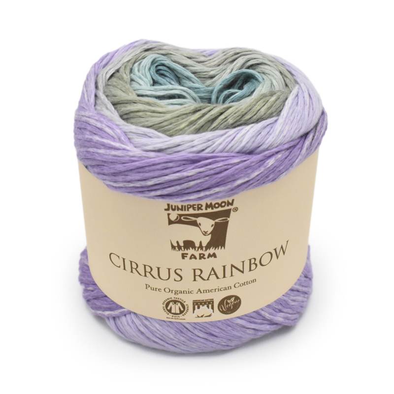 A skein of Juniper Moon Farm Cirrus Rainbow yarn, featuring a variegated color pattern of lavender, light purple, sage green, and light blue, wrapped in a beige paper label.