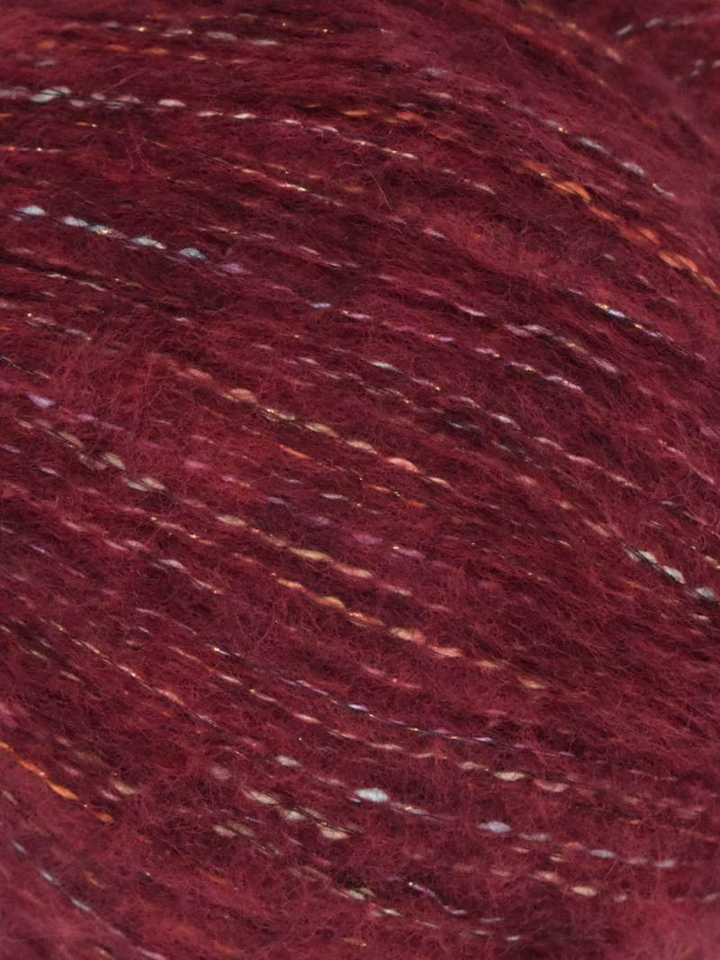 A close-up of maroon yarn with subtle variegated flecks of white, orange, and gold threading through the fibers.