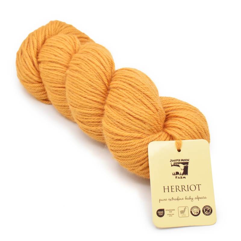 A skein of mustard yellow yarn with a cream-colored paper tag attached, photographed on a clean white background. The tag is branded 'Jolly Roger Fabrics' and labeled 'Herriot'.