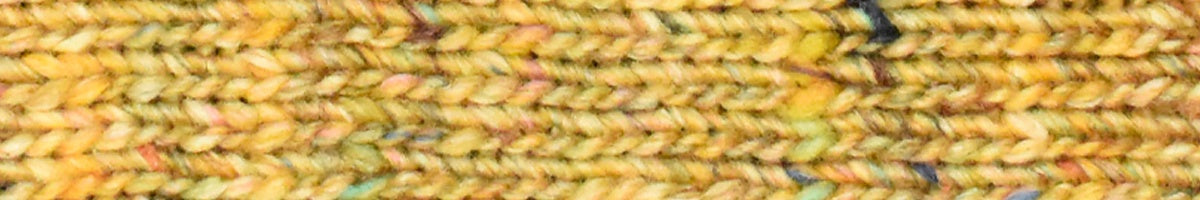 A close-up texture shot of a chunky knit fabric in a variegated blend of mustard yellow, beige, orange, and soft pink yarn.
