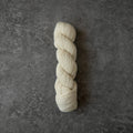 A skein of cream-colored yarn standing vertically on a textured dark gray surface.