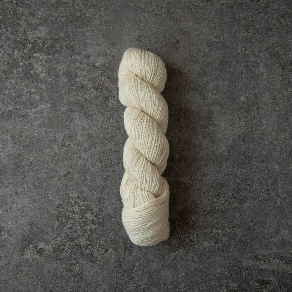 A skein of cream-colored yarn standing vertically on a textured dark gray surface.