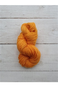 A skein of bright orange yarn resting on a light gray wooden plank surface.