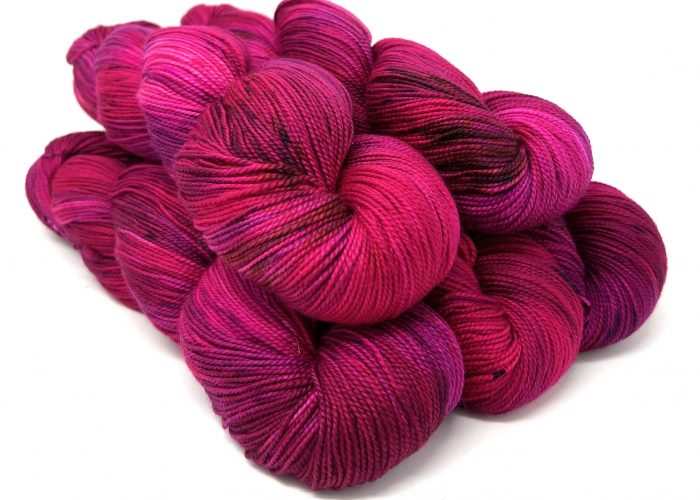A pile of hanks of variegated yarn in shades of magenta, fuchsia, and deep purple on a white background.