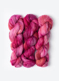 Three skeins of pink and red yarn on a white background