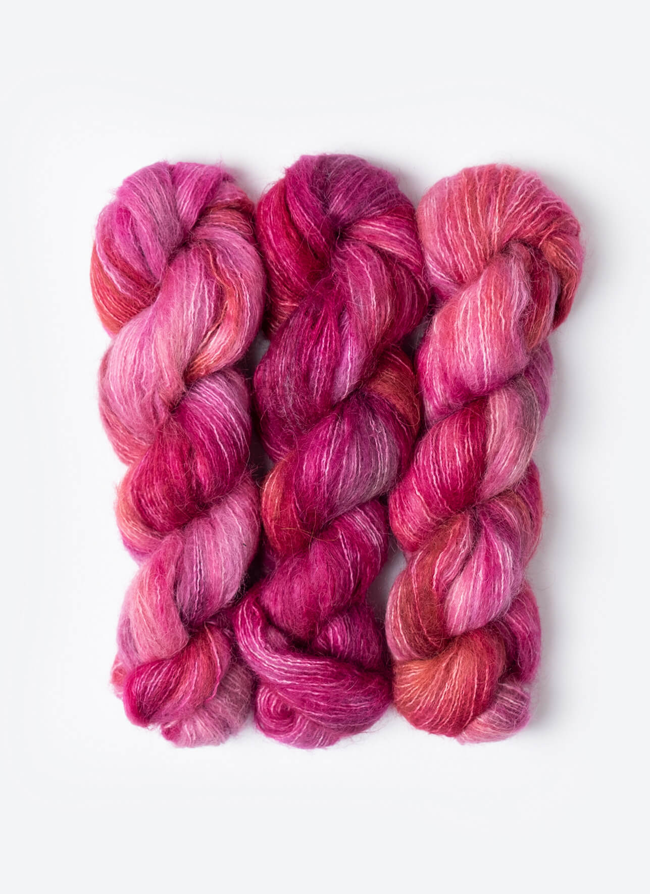 Three skeins of pink and red yarn on a white background