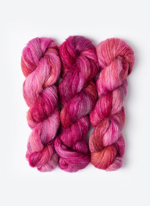 Three skeins of pink and red yarn on a white background