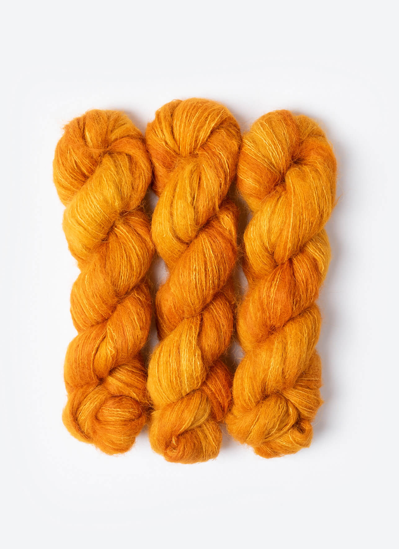Three skeins of orange yarn on a white background