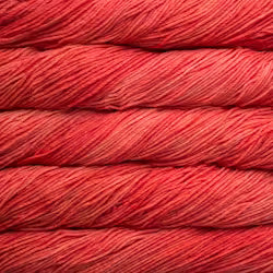 A close-up of tightly wound yarn skeins in a warm coral-red color, filling the entire frame.