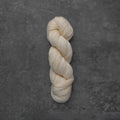 A single twisted skein of cream-colored yarn placed vertically on a textured dark gray surface.