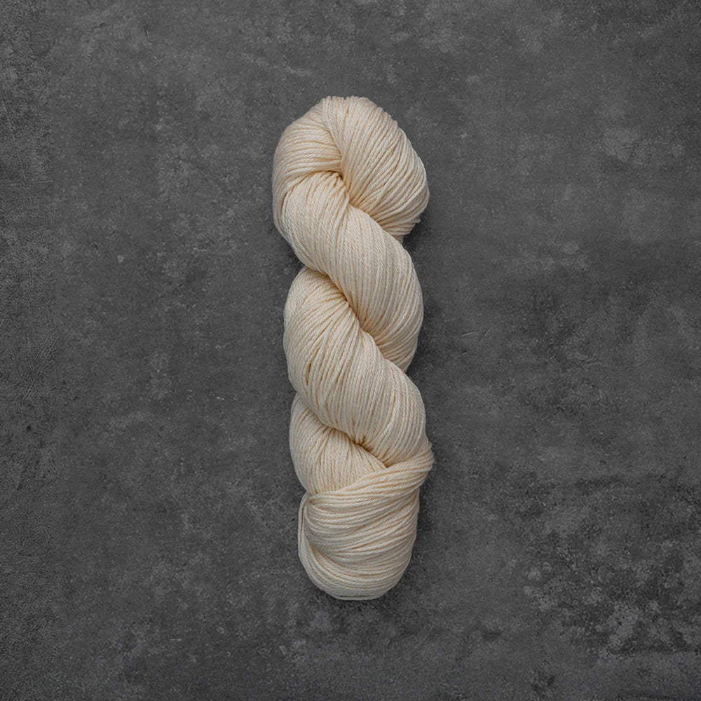 A single twisted skein of cream-colored yarn placed vertically on a textured dark gray surface.