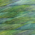 A close-up of textured yarn strands in a variegated blend of green, yellow, and blue, arranged horizontally.