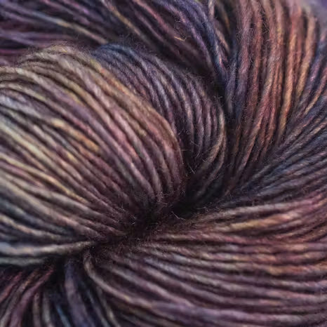 A close-up of variegated yarn with blended dark purple, brown, and warm beige tones, showing the soft texture of the fibers.